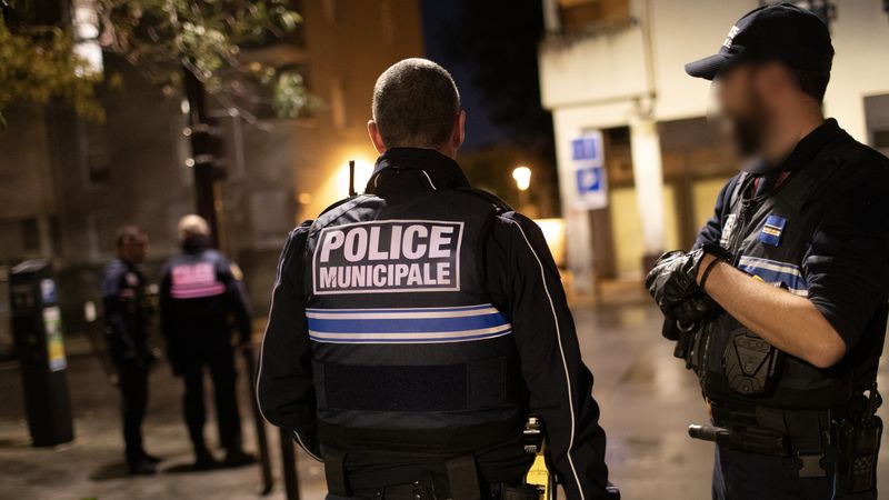 Place de la Galarne. La place, plongée dans l’obscurité, est calme. Légèrement à l’écart, un individu, capuche sur la tête, observe les allées et venues des forces de l’ordre. Équipés de lampes torches, les policiers fouillent les parterres de fleurs. Ces derniers « servent à dissimuler de la drogue », explique Cédrik Pitrosky. Konrad surveille les étages des immeubles alentours, prêt à mettre son bouclier en opposition.  « Ce dernier est un vrai plus pour nous protéger car nous recevons souvent des projectiles. On vient perturber le trafic, ça déplaît... », témoigne ce jeune agent à la stature d’athlète. Il continue : « La plus grande qualité d’un policier municipal, c’est la patience ». © Ludovic Failler